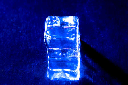 Photo of one blue ice cube and its reflection