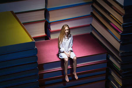 Thinking small young woman sitting on big booksの写真素材