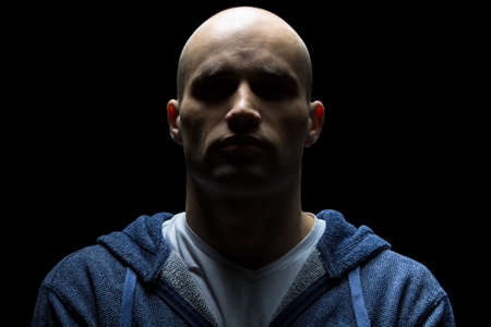 Photo of young hairless man in shadow on black backgroundの写真素材