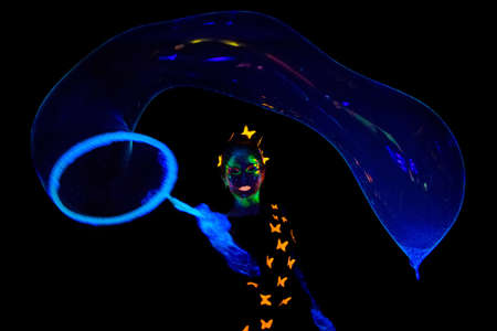 Photo of young  woman with luminous make up with big bubble in darkness