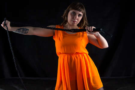 Image of woman in orange dress with whip on black background