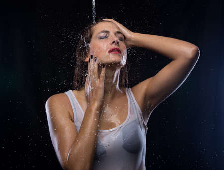 Wet woman under stream of water on black backgroundの写真素材