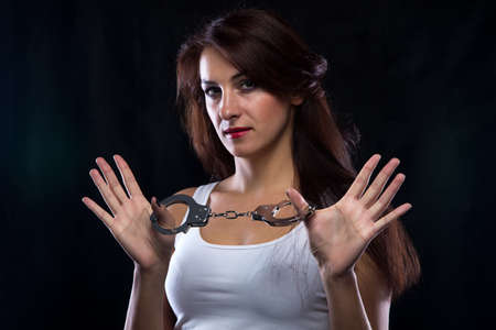 Woman in white t-shirt with handcuffs. Portrait photo with black background.の写真素材