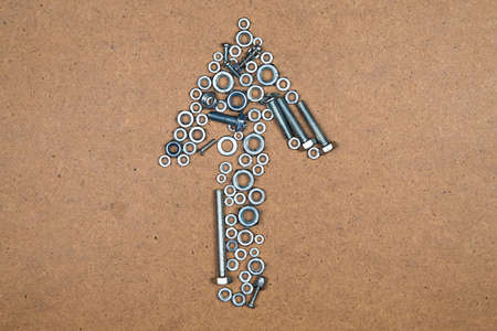 Up arrow from bolts and nuts. Photo of mozaic sign on wood background.