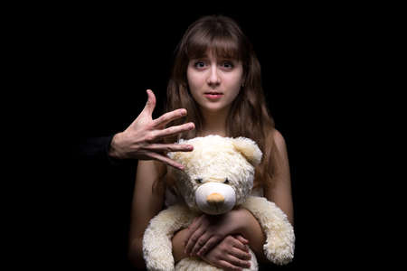 Fearful teenage girl with toy on black background