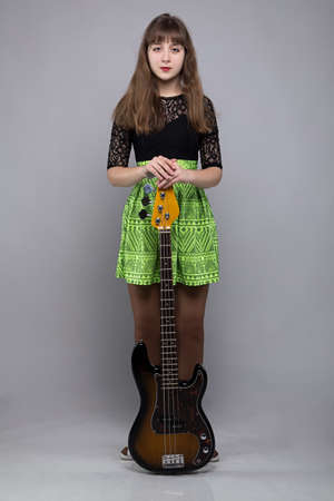 Teenage girl in dress with guitar on grey backgroundの写真素材