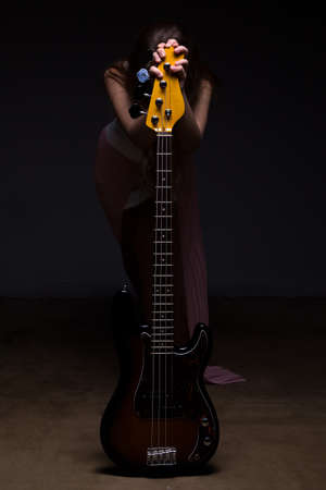Hidden teenage girl behind guitar on black backgroundの写真素材
