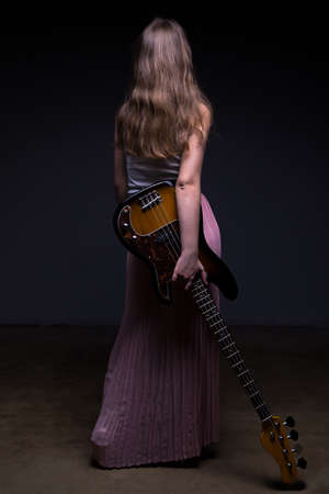Teenage girl with guitar, from back on black backgroundの写真素材