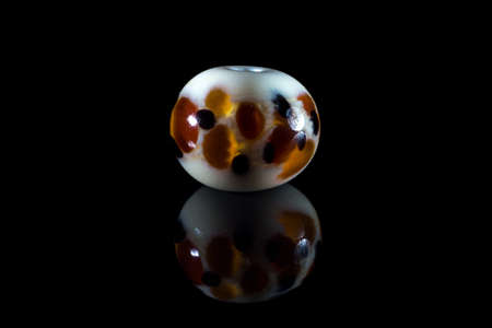 White and brown glassy bead with reflection on black backgroundの写真素材