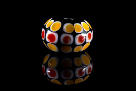 Yellow and red glassy bead with reflection on black background