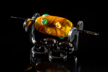 Yellow glass bead on stand on black backgroundの写真素材