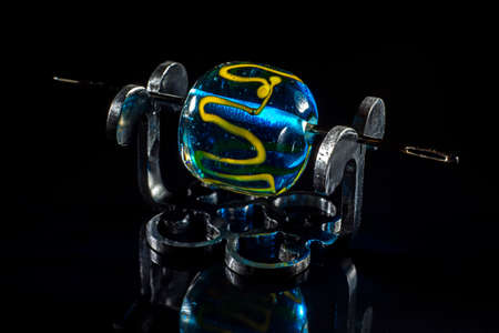 Blue and yellow glass bead on stand on black background