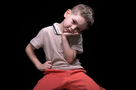 Little tired boy with hands on hips on black background