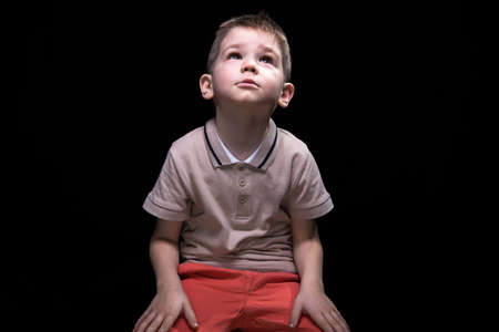 Sitting little boy looking up on black backgroundの写真素材