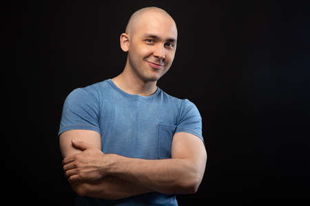 Photo of smiling bald man in blue tee shirt with arms crossed