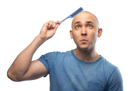 Photo of young bald man in blue tee shirt with hairbrushの写真素材