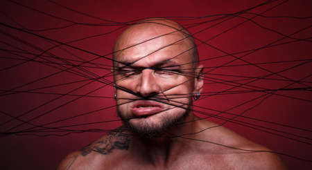 Photo of tangled in threads bald man on red backgroundの写真素材