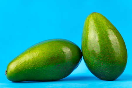 Image of two ripe fresh green avocado on blue background