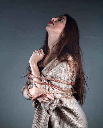 Photo of young binded girl with rope on sweater on grey background