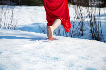 Photo of barefoot woman in a red dress walking on snowの写真素材
