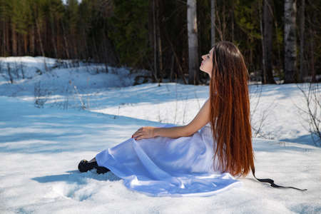 Shot of girl in a white dress sitting on snowの写真素材