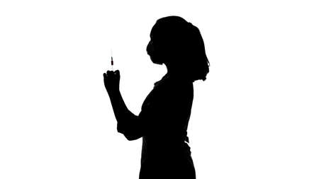 Photo of womans silhouette in mask with syringe in profileの写真素材