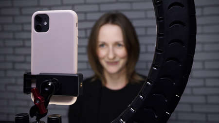 Photo of blogger woman shooting story with ring lamp on brick wall backgroundの写真素材