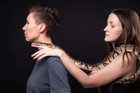 Photo of two women with python on shoulders in profileの写真素材