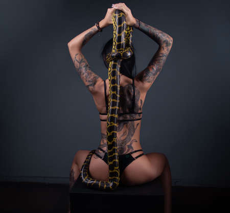 Photo of the sitting woman from back holding anaconda along the spineの写真素材