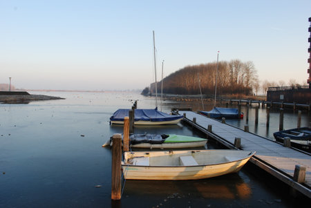 Boats moored to a pier on a frozen lake in winterの写真素材