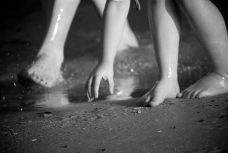 a mother's feet and her child's feet and hand in the sand at the beach in black and whiteの写真素材
