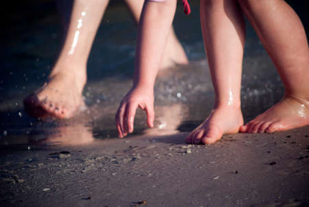 a mother's feet and her child's feet and hand in the sand at the beachの写真素材