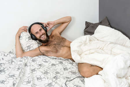 young man is listening music with a headphone in his bedの写真素材