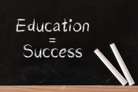 Education is success concept on blackboard with two white chalks.の写真素材