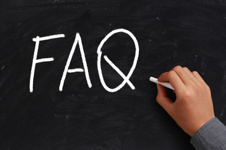 FAQ written on black chalkboard with white chalk in hand.の写真素材