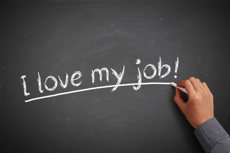 Hand with white chalk writing 'I love my job!' on chalkboard.の写真素材