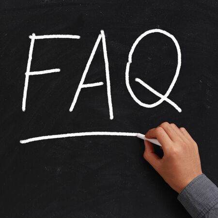 FAQ written on black chalkboard with white chalk in hand.の写真素材