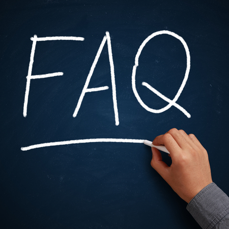FAQ written on blue chalkboard with white chalk in hand.の写真素材