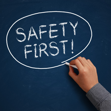 Hand with white chalk writing 'Safety First!' on chalkboard.の写真素材