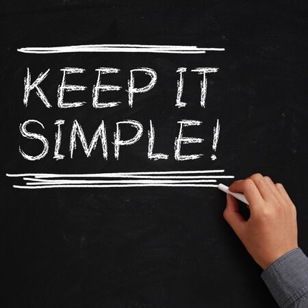 Hand with white chalk writing 'Keep it simple!' on chalkboard.の写真素材