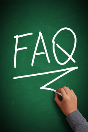 FAQ written on green chalkboard with white chalk in hand.の写真素材