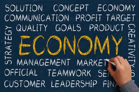Economy word cloud is written on blue chalkboard by the hand of a businessman.の写真素材