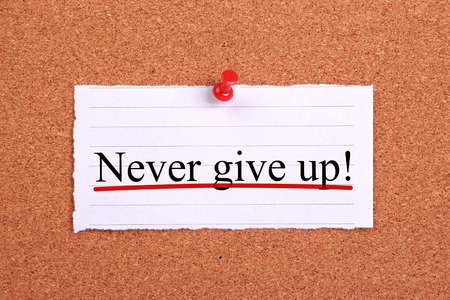 Never give up text paper is pinned on cork.の写真素材