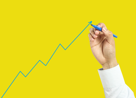 Businessman is drawing growth graph with marker on transparent board with yellow background.の写真素材