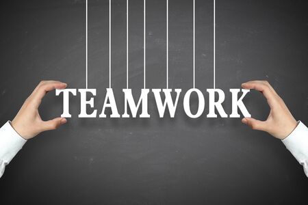 Businessman is holding the Teamwork text against the blackboard background.の写真素材