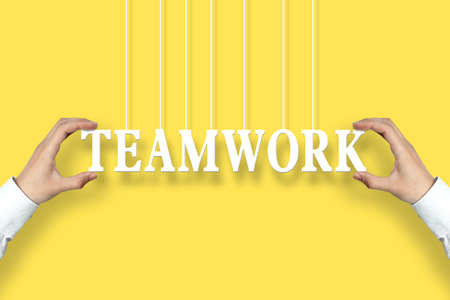 Businessman is holding the Teamwork text against the yellow background.の写真素材