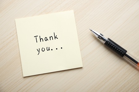 A yellow sticky note is written something on the desk with a ball pen aside.の写真素材