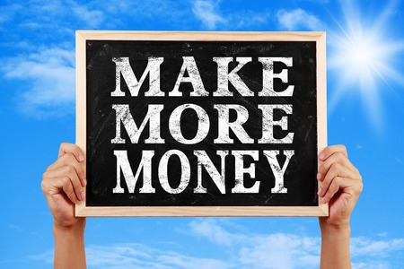 Hands holding blackboard with text Make More Money against blue sky background.の写真素材