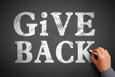 Hand with chalk is writing the concept of Give Back on the blackboard.