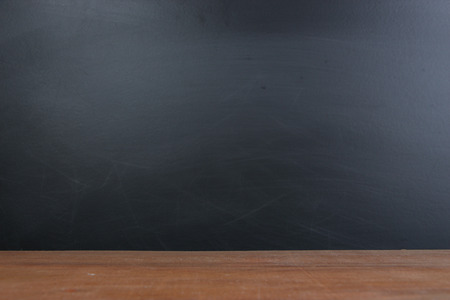Blank blackboard background with wooden desk in front.